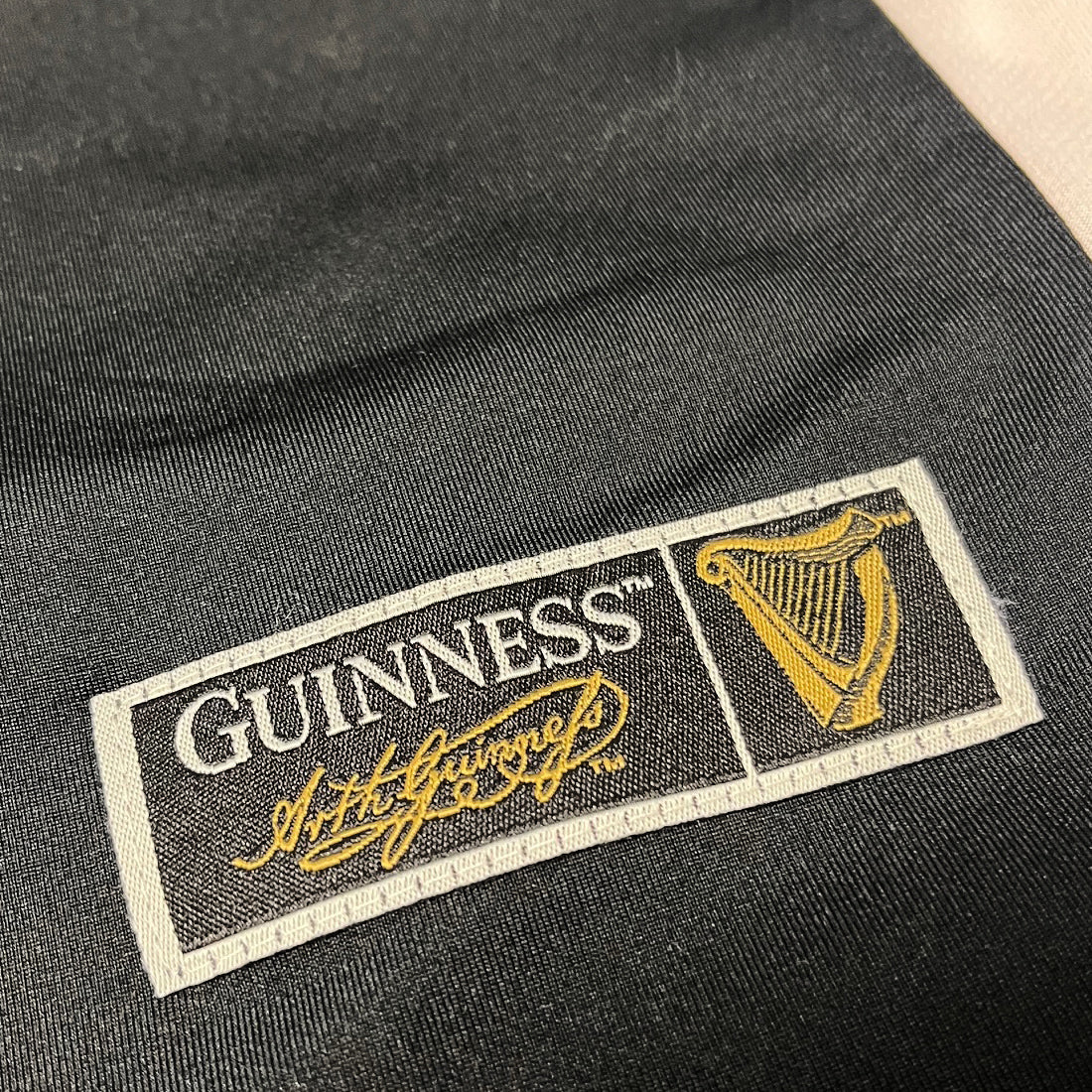 Guinness patch label on dark fabric displaying the logo, gold signature, and harp emblem