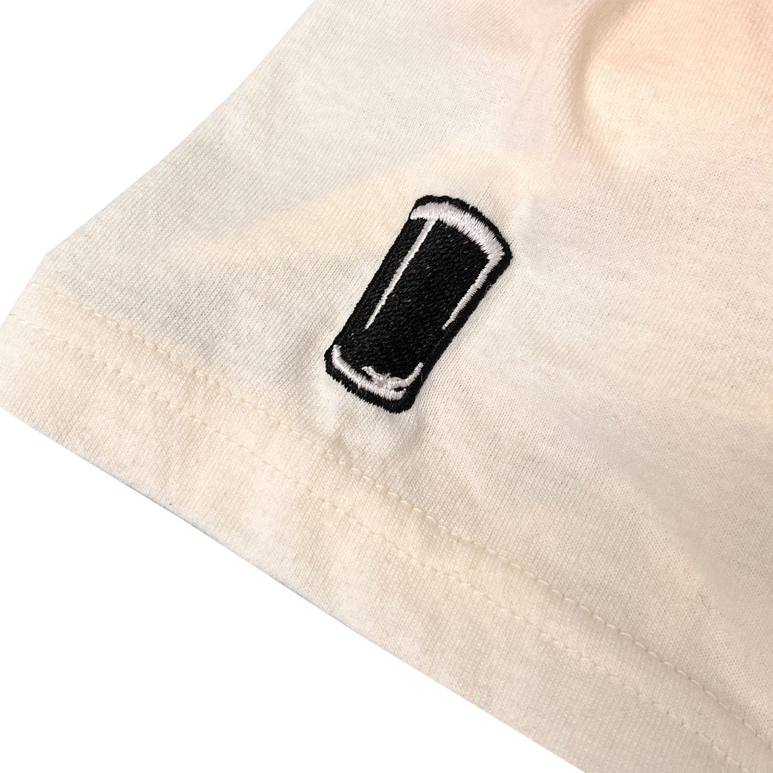 Close-up of a cream T shirt sleeve showing a small black rectangular embroidered patch