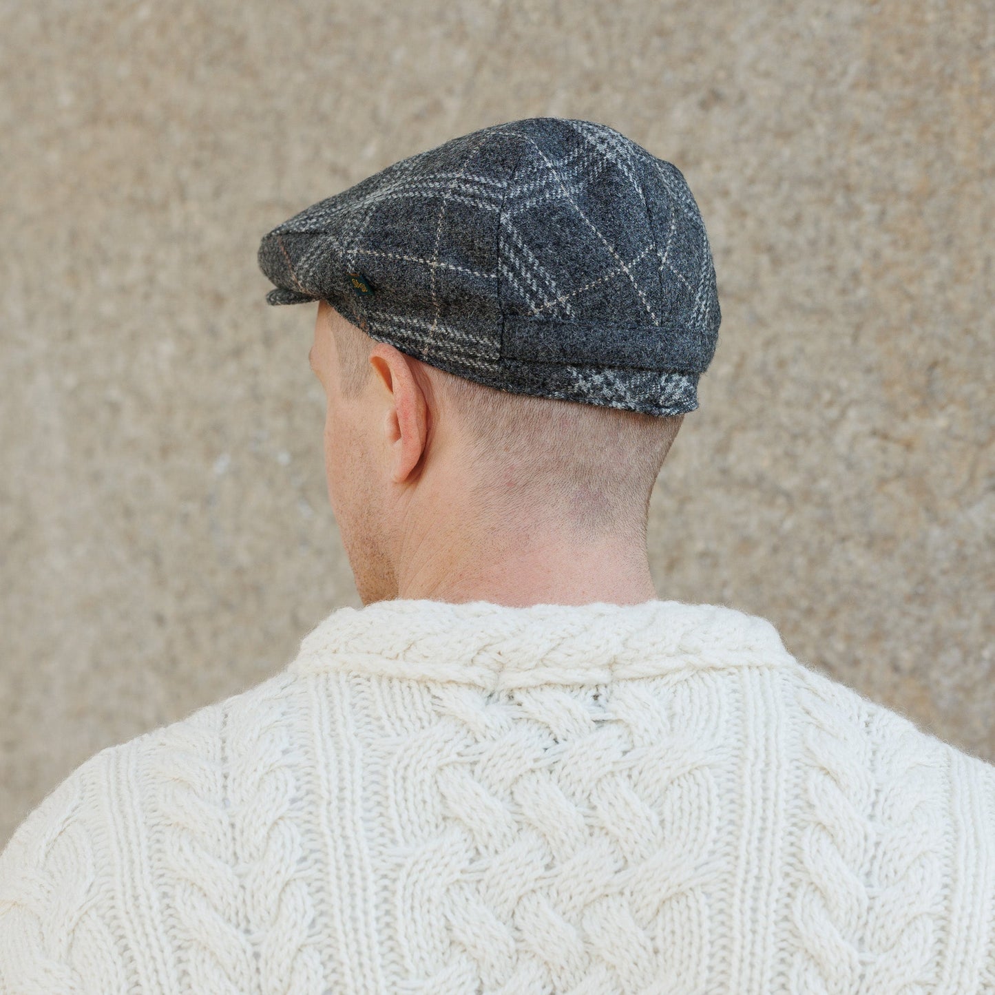 Back view of person wearing gray plaid flat cap and white cable knit sweater