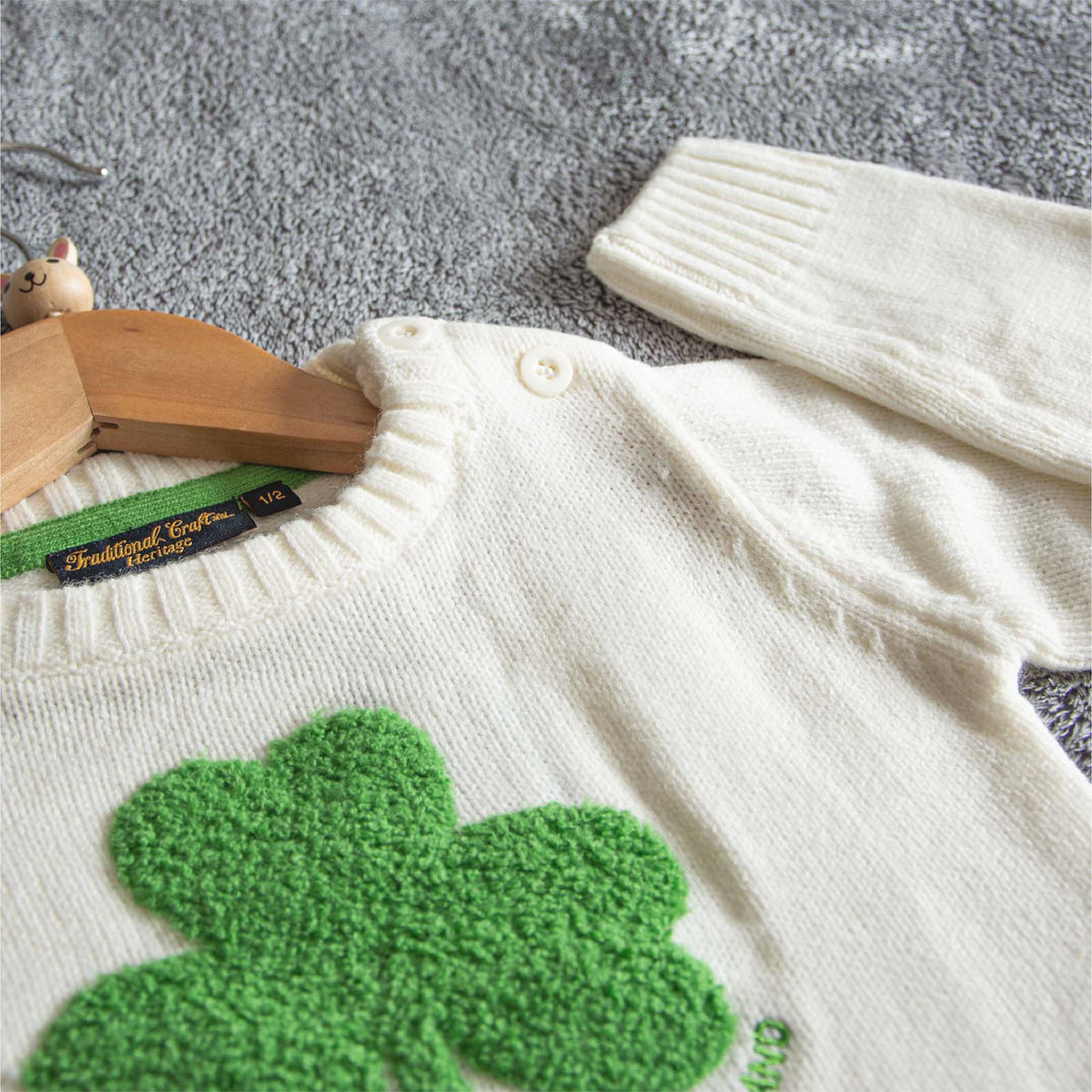 Close up of the cream sweater showing the textured green shamrock applique on the chest.