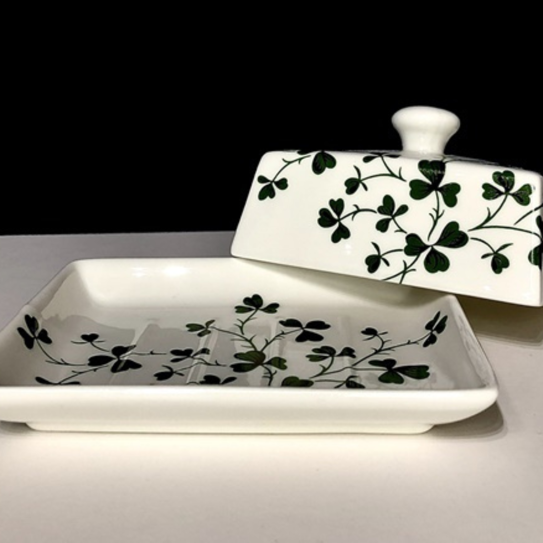 Open white ceramic shamrock butter dish with lid nearby displaying the green leaf pattern.