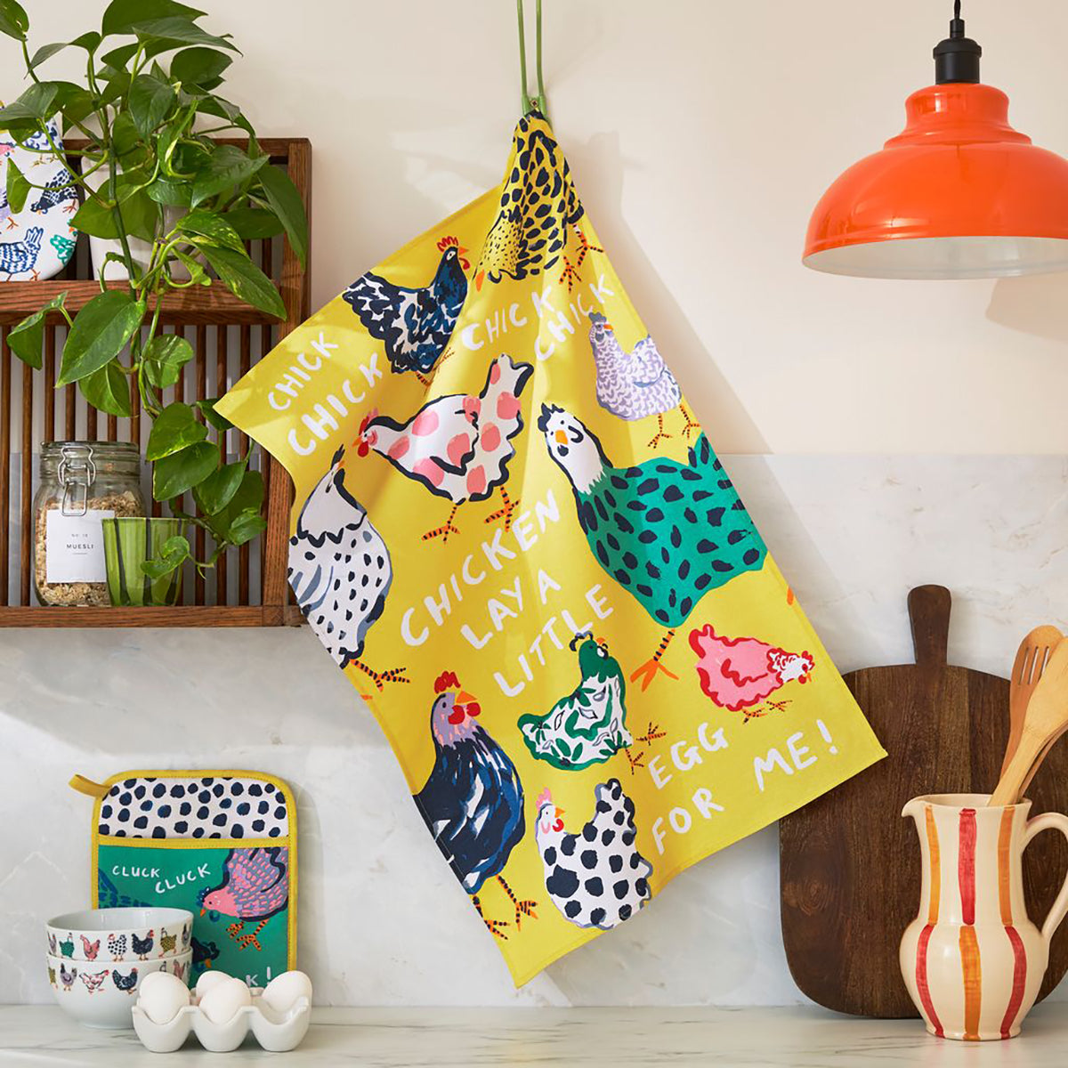 Bright yellow Chick Chicken cotton tea towel with colorful chickens hanging in a kitchen setting