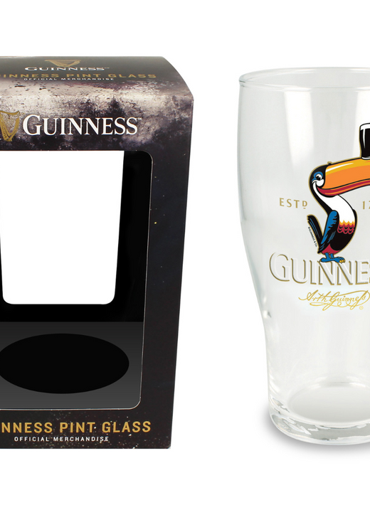 Clear pint glass with colorful toucan and Guinness logo beside black packaging