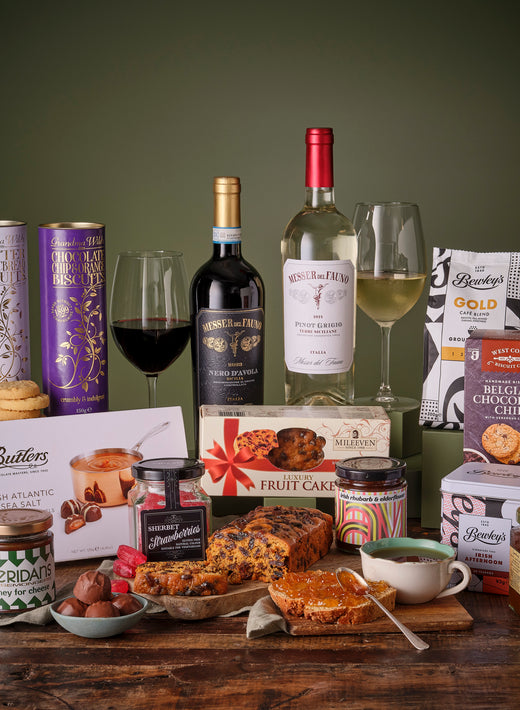 Classic Irish food and wine gift basket with two wine bottles, biscuits, chocolates, and tea among gourmet items.
