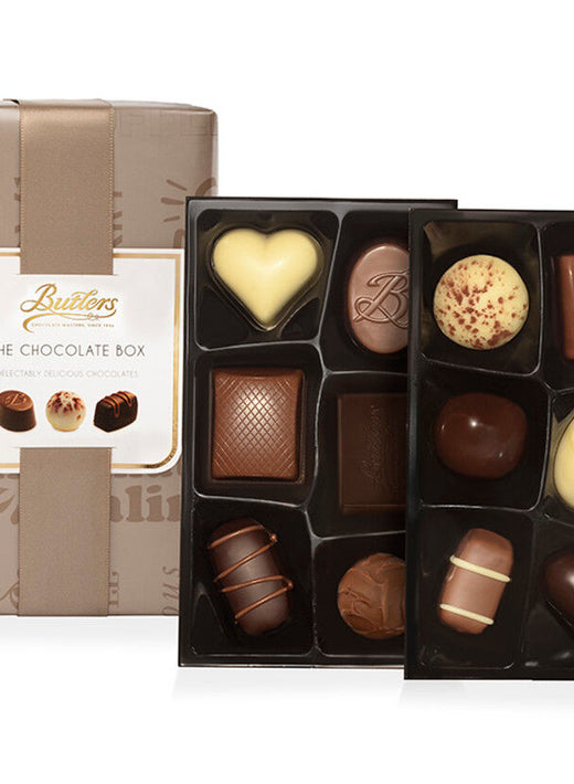 Two trays of assorted chocolates next to a beige wrapped chocolate box