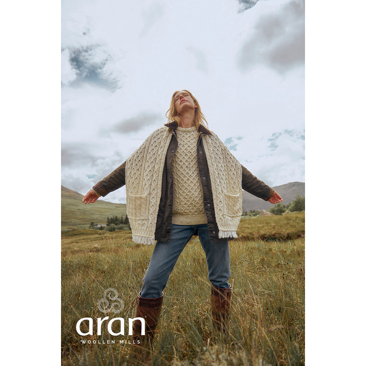 Cream Shannon Merino Aran wrap worn by a woman in an open field with arms outstretched and fringe hem.