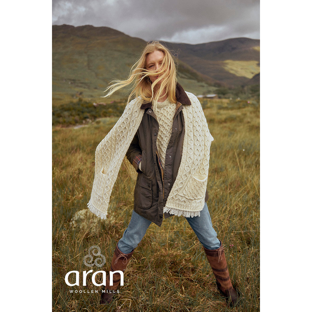 Model outdoors wearing cream Shannon Merino Aran wrap draped over shoulders in a grassy landscape