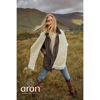 Model outdoors wearing cream Shannon Merino Aran wrap draped over shoulders in a grassy landscape