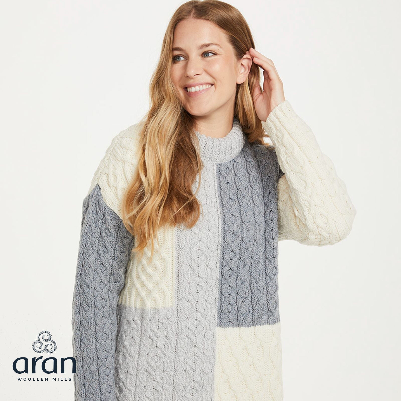 Smiling woman in a color block patchwork cable knit sweater with a ribbed high collar.