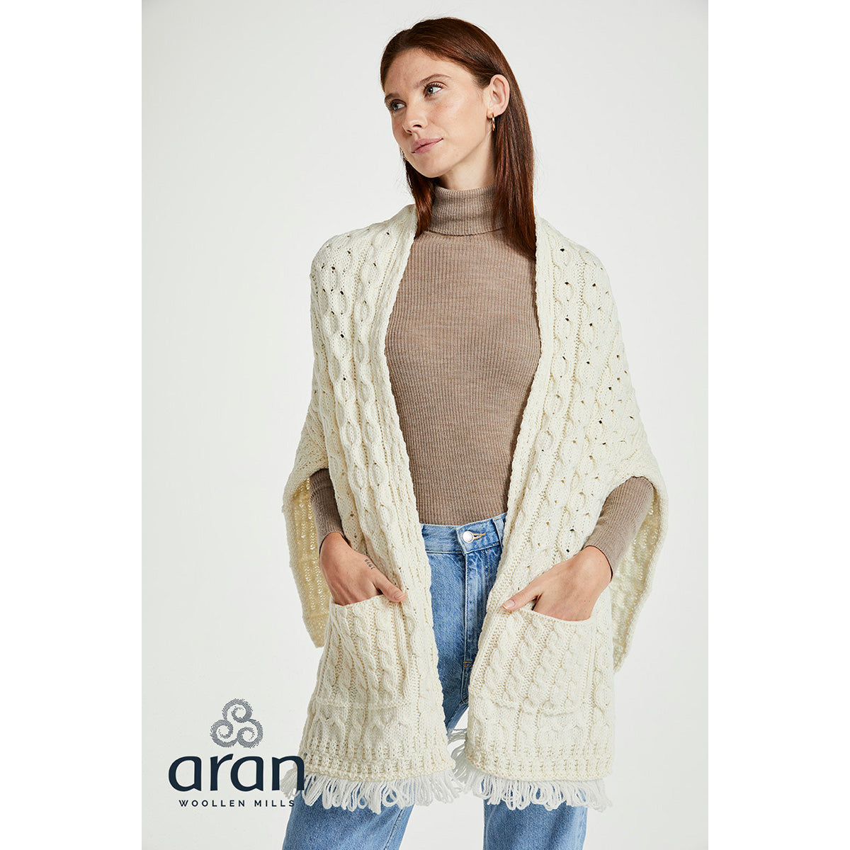 Model wearing cream Shannon Merino Aran wrap over taupe turtleneck and jeans with fringed hem