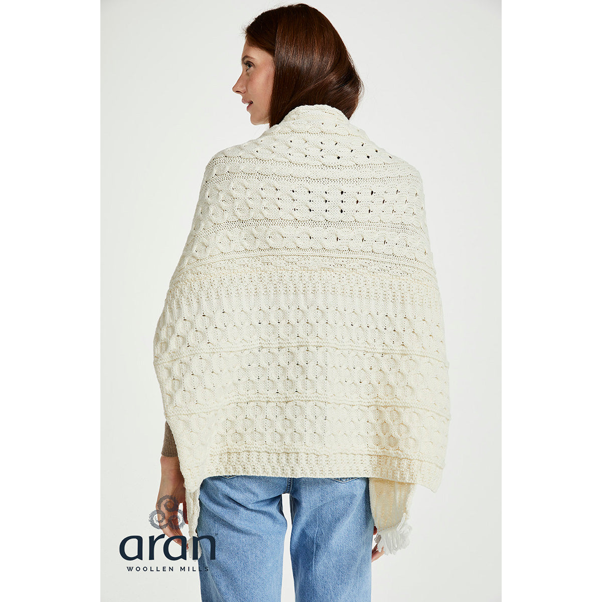 Back view of cream Shannon wrap draped over shoulders, showcasing knitted pattern and fringe hem.