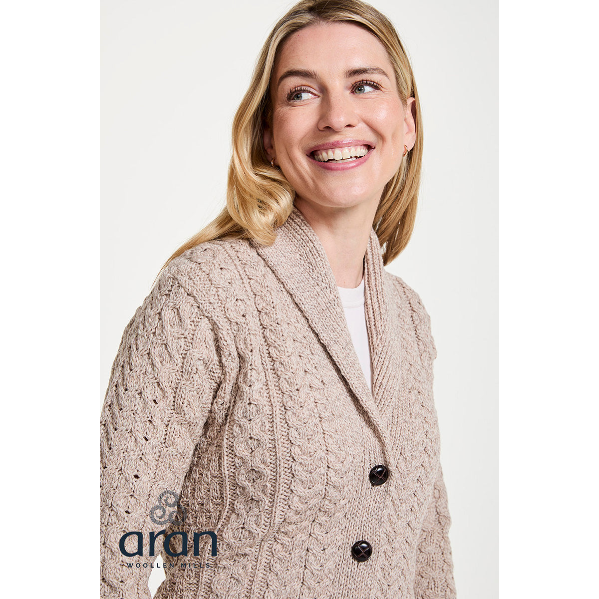 Close-up of a smiling woman wearing a beige textured knit shawl collar cardigan.