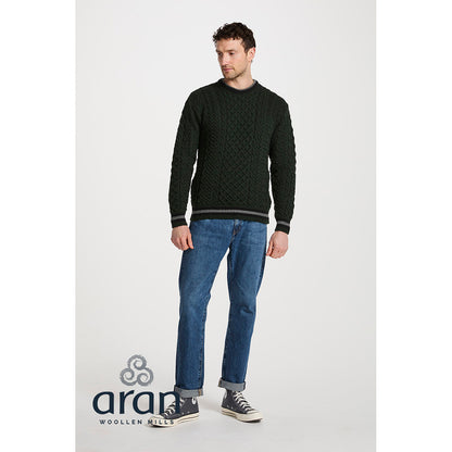 Man modeling a dark green Merino Aran crewneck sweater with cable knit pattern and striped hem and cuffs.