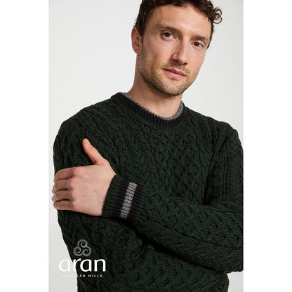Male model wearing Inishbeg Stripe Crewneck Merino Green Aran Sweater with dark cable knit and gray striped cuffs