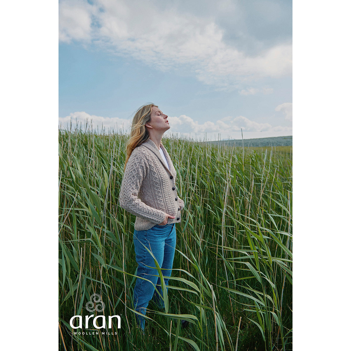 Womens Tourmakeady Shawl Collar Merino Aran Cardigan worn by a model in a field among tall grasses.