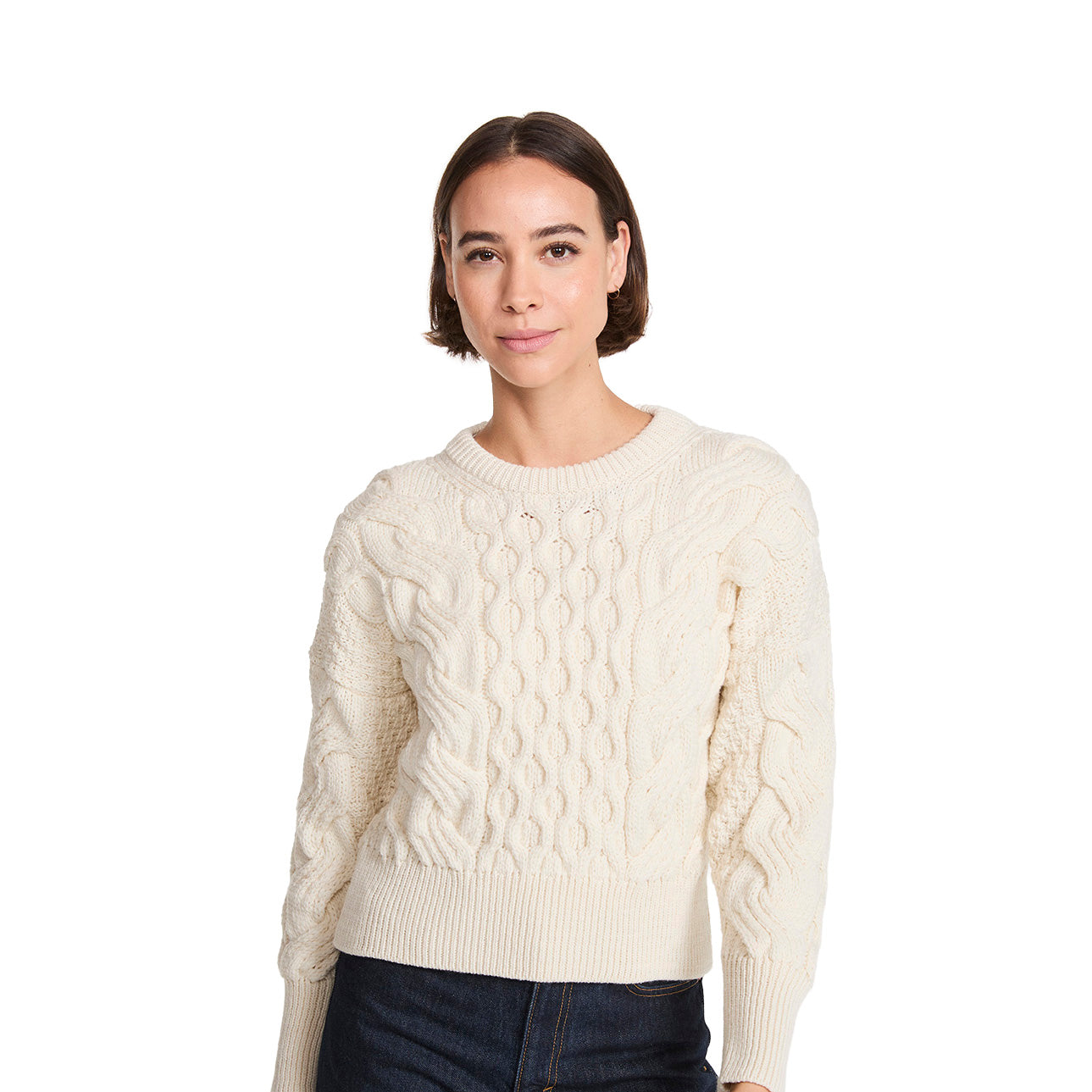 Model wearing cream cropped cable knit sweater with a chunky knit pattern and ribbed hem, paired with dark jeans.