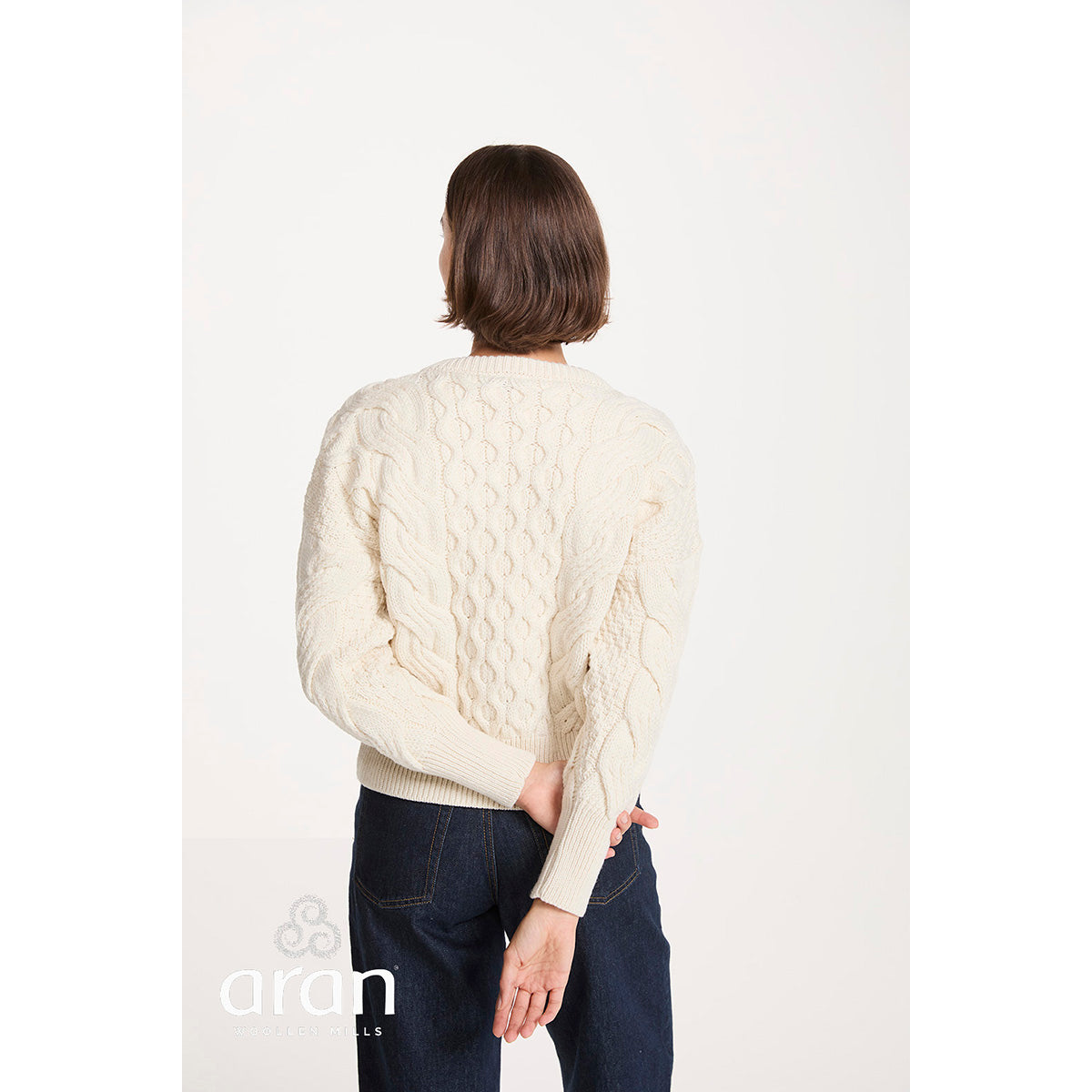 Back view of a cream cropped cable knit sweater worn by a model
