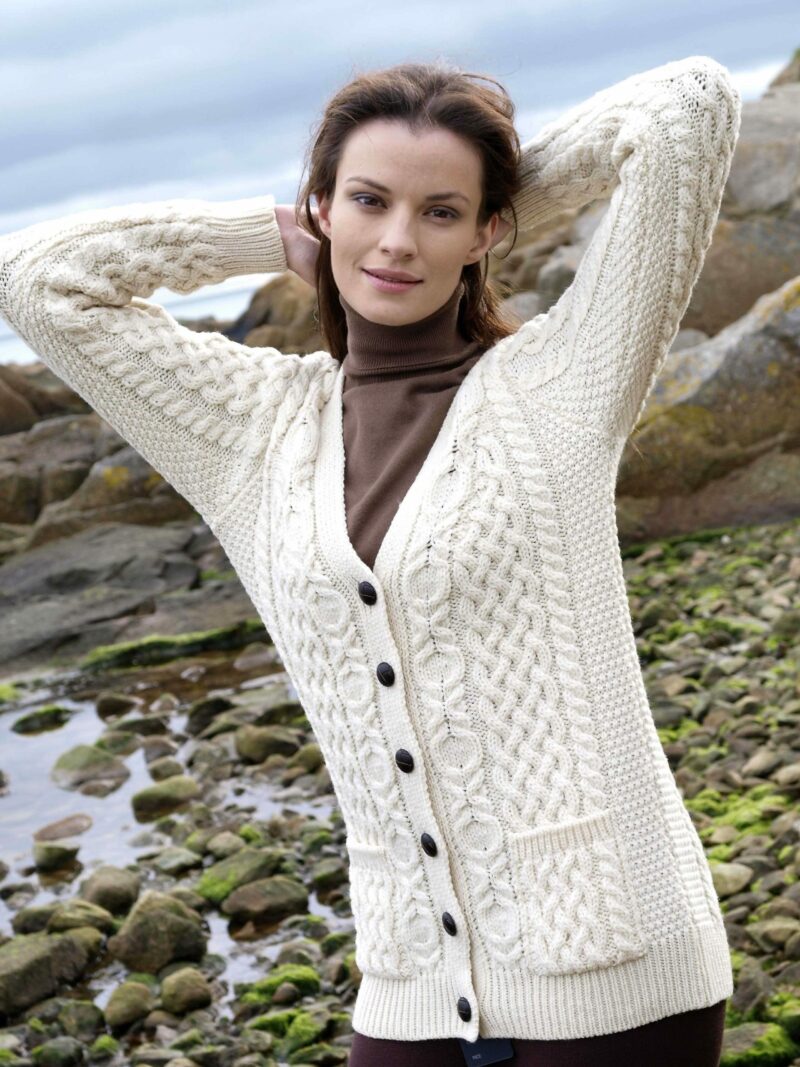 Cream Aran cardigan with cable knit and button front worn by a model by a rocky shore.