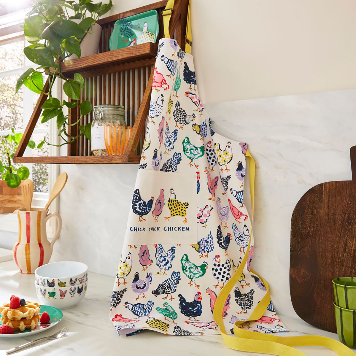 Chick Chicken cotton apron with colorful chicken print hanging in a bright kitchen.