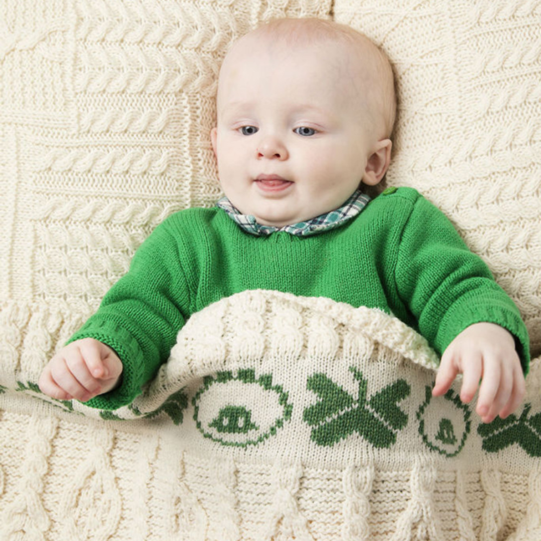 Baby lying on knitted blanket wearing green sweater and plaid collar