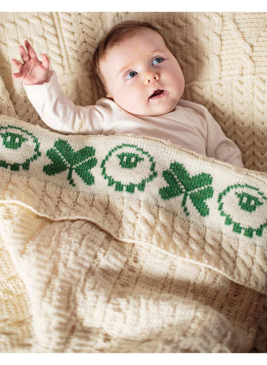 Baby lying on knitted blanket with green clover and sheep patterns