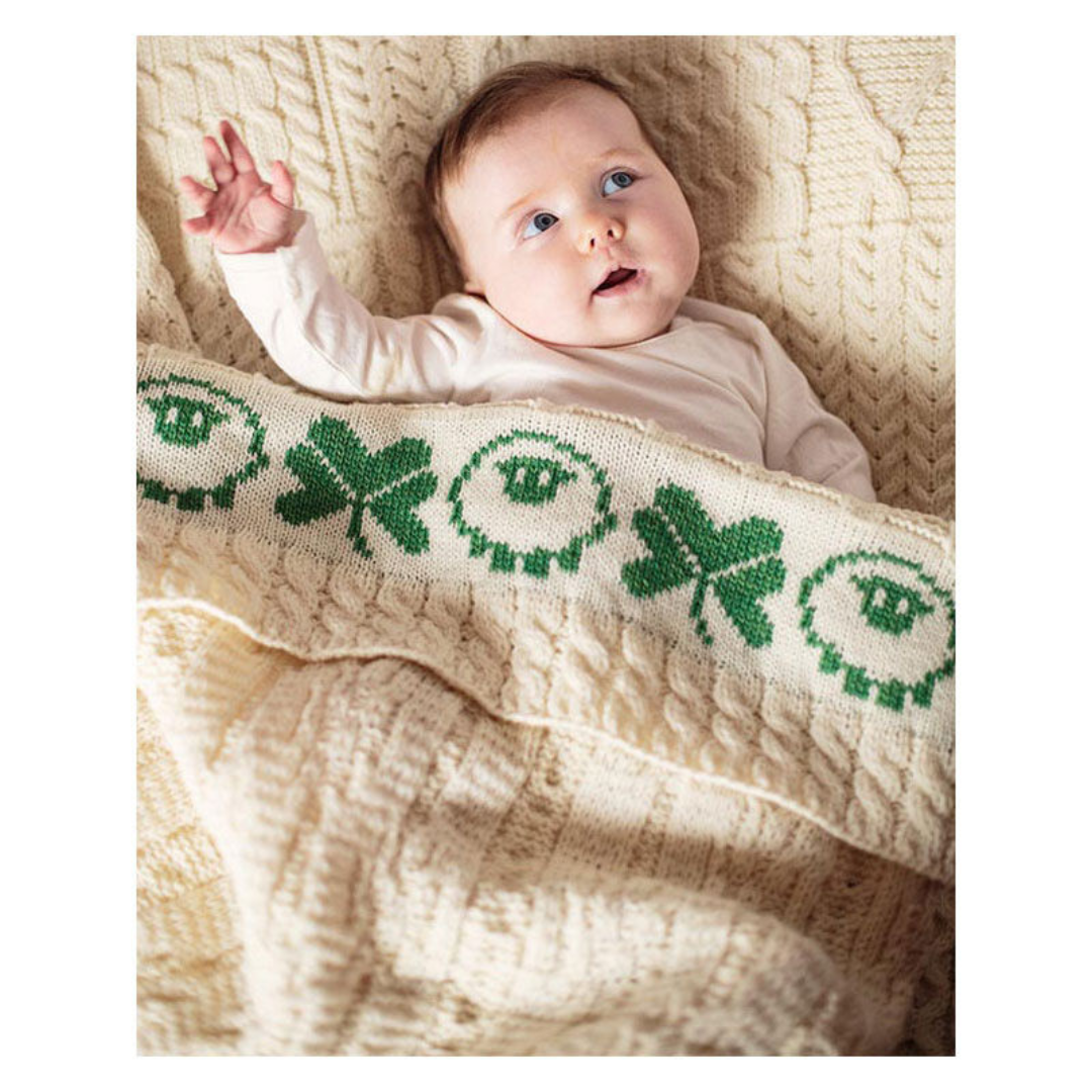 Baby lying on knitted blanket with green clover and sheep patterns