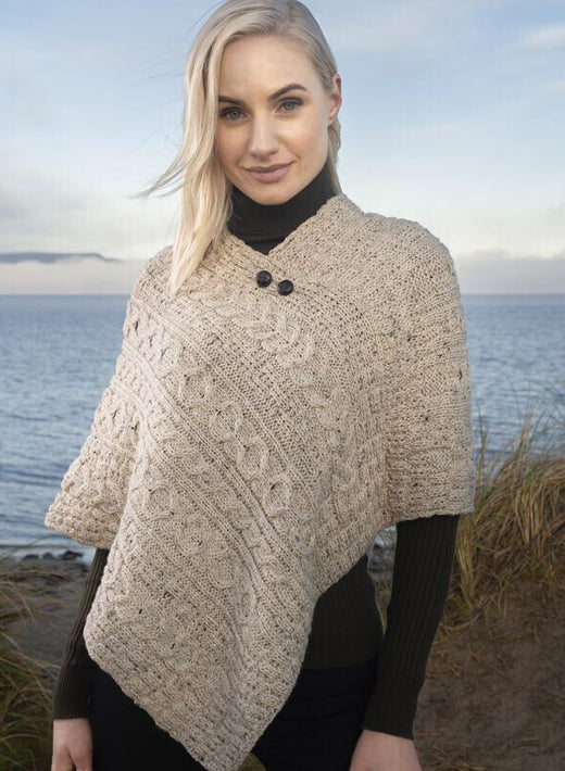 Blonde woman wearing beige knitted poncho standing by the sea shore