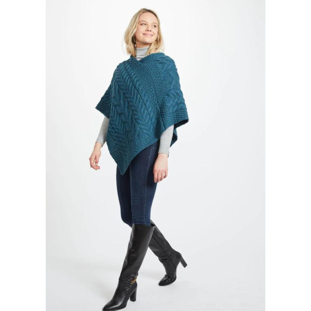 Woman wearing a teal knitted poncho, gray top, jeans, and black boots