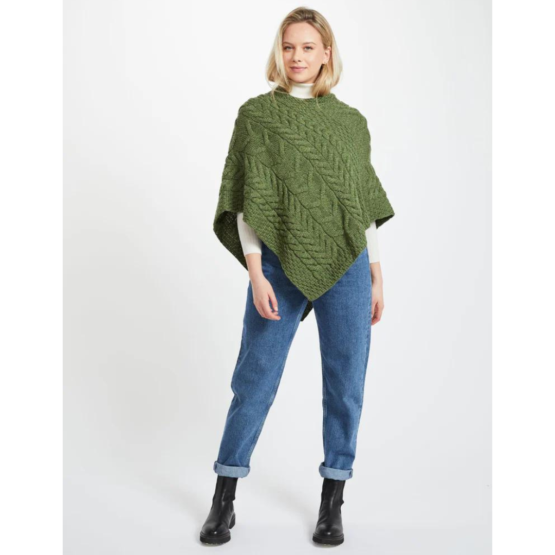 Woman wearing green knitted poncho, blue jeans, and black boots