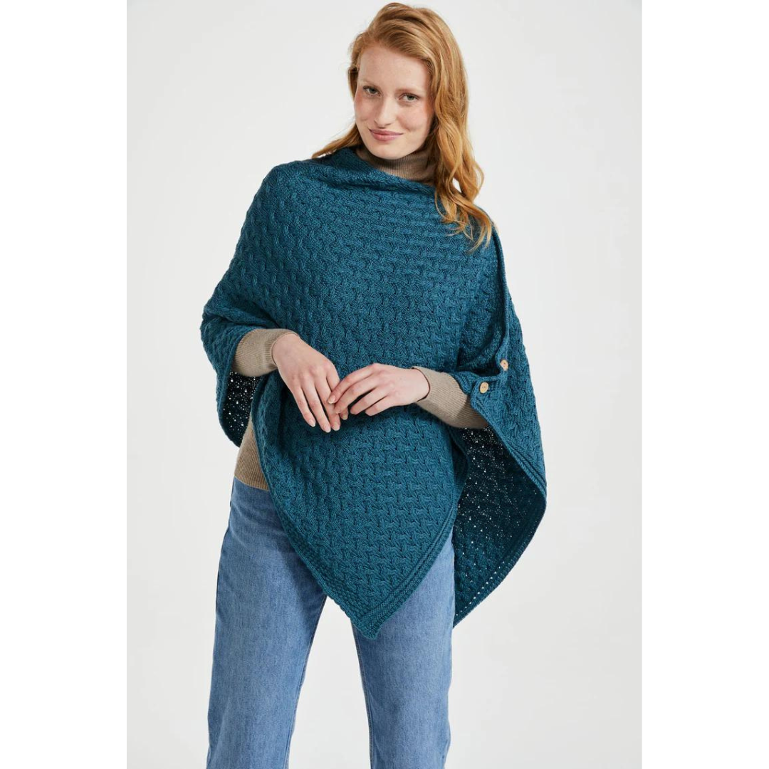 Woman wearing teal knitted poncho over beige sweater and blue jeans