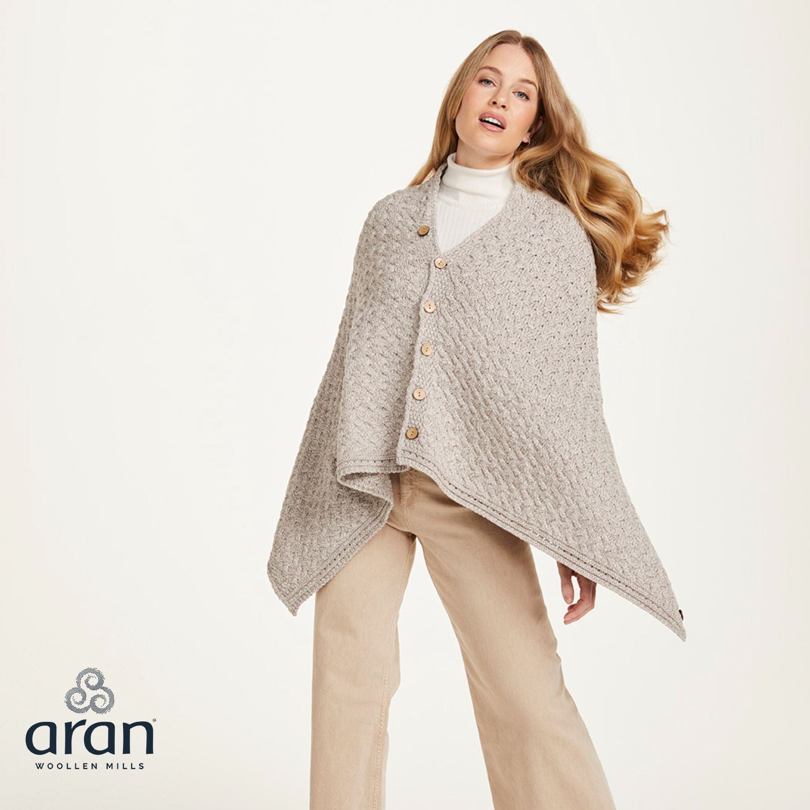 Woman wearing a beige knitted buttoned poncho with beige pants