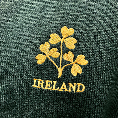 Close up of gold shamrock embroidery on dark green knit with IRELAND text.