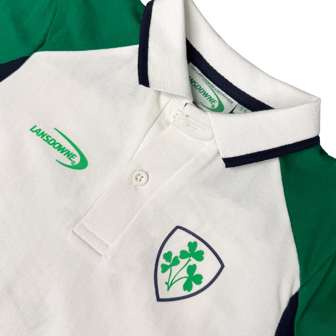 Close up of Lansdowne Ireland kids polo shirt with white body green sleeves navy trimmed collar and a shield crest on the chest