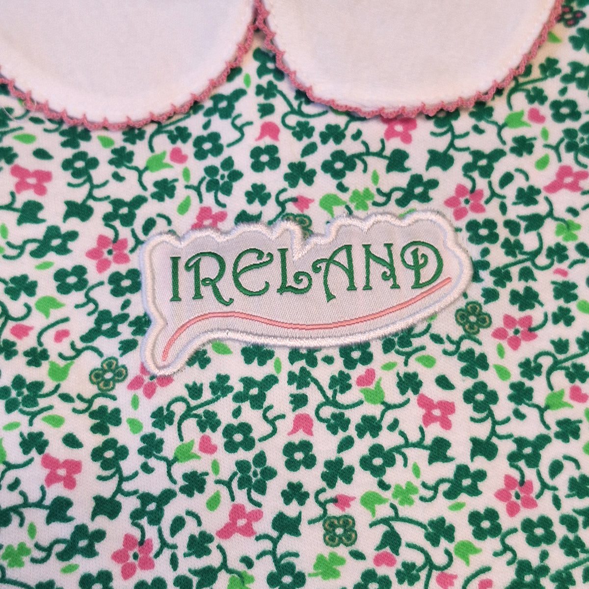 Close up of floral fabric with Ireland patch and pink trimmed collar on the vest