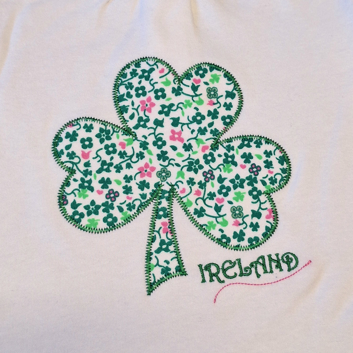 Close-up of a shamrock shaped applique with green and pink floral print on white fabric.