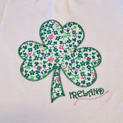Close-up of a shamrock shaped applique with green and pink floral print on white fabric.