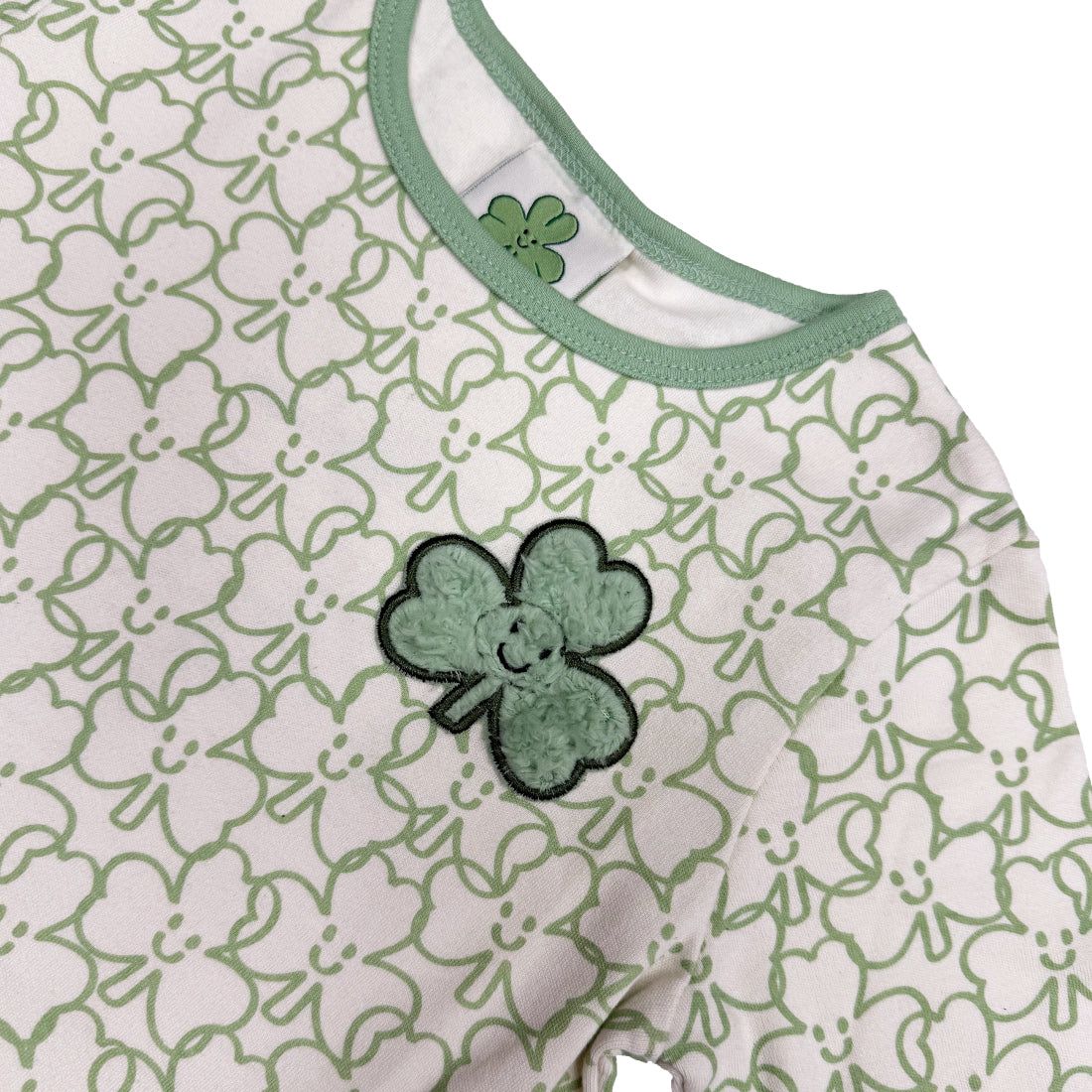 Close-up of a kid's long sleeve dress with white and green shamrock print and green neckline trim