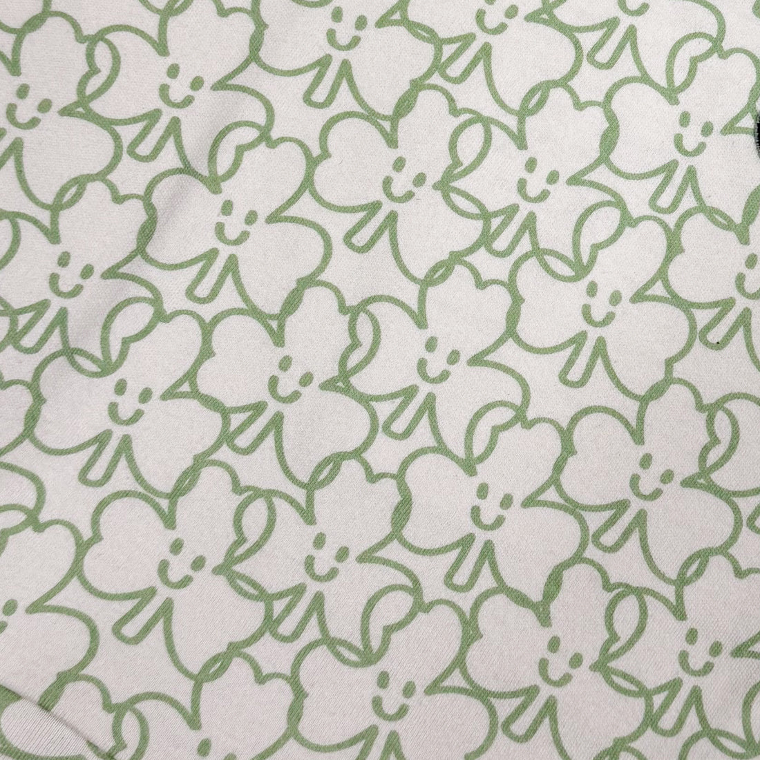 Fabric close-up showing white background with green shamrock outline print used on the dress