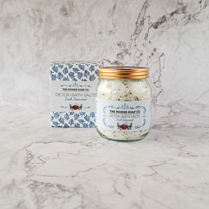 The Moher Soap Co Irish Seaweed Detox Bath Salts jar with a gold lid beside its blue patterned box on a marble surface.