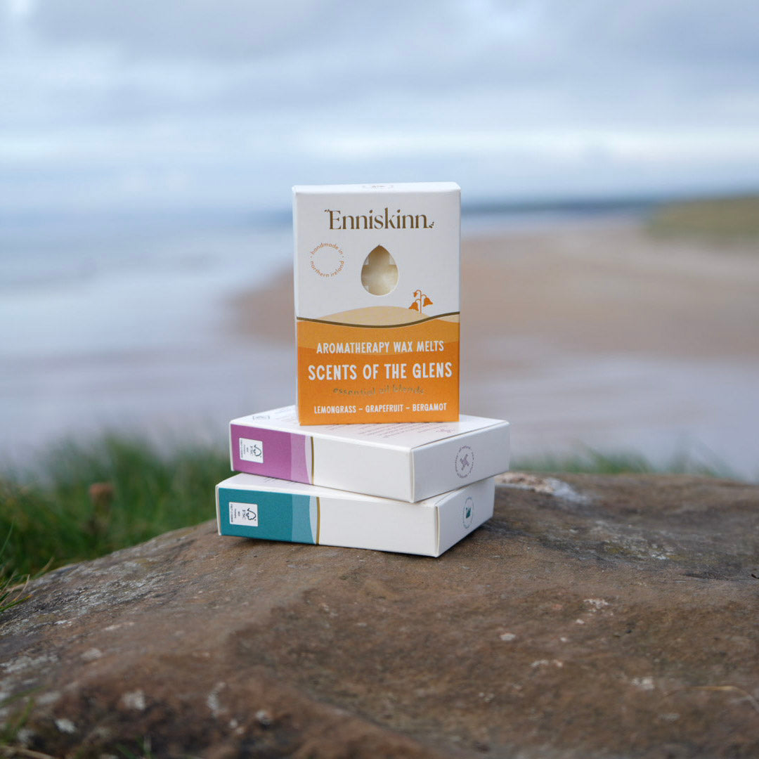Enniskinn Scents of the Glens aromatherapy wax melts box perched on a stack of three boxes against a coastal backdrop.