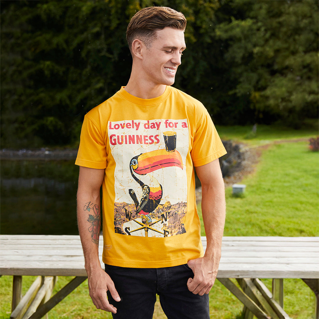Man wearing a yellow Guinness Lovely Day Toucan Golden T-Shirt with toucan graphic outdoors