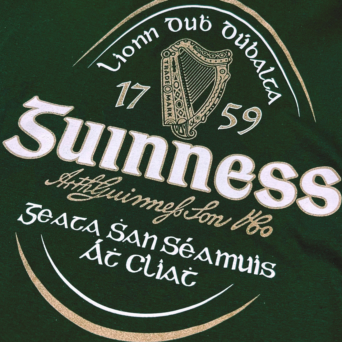 Close up of Guinness logo on dark green T shirt showing harp and crest details.