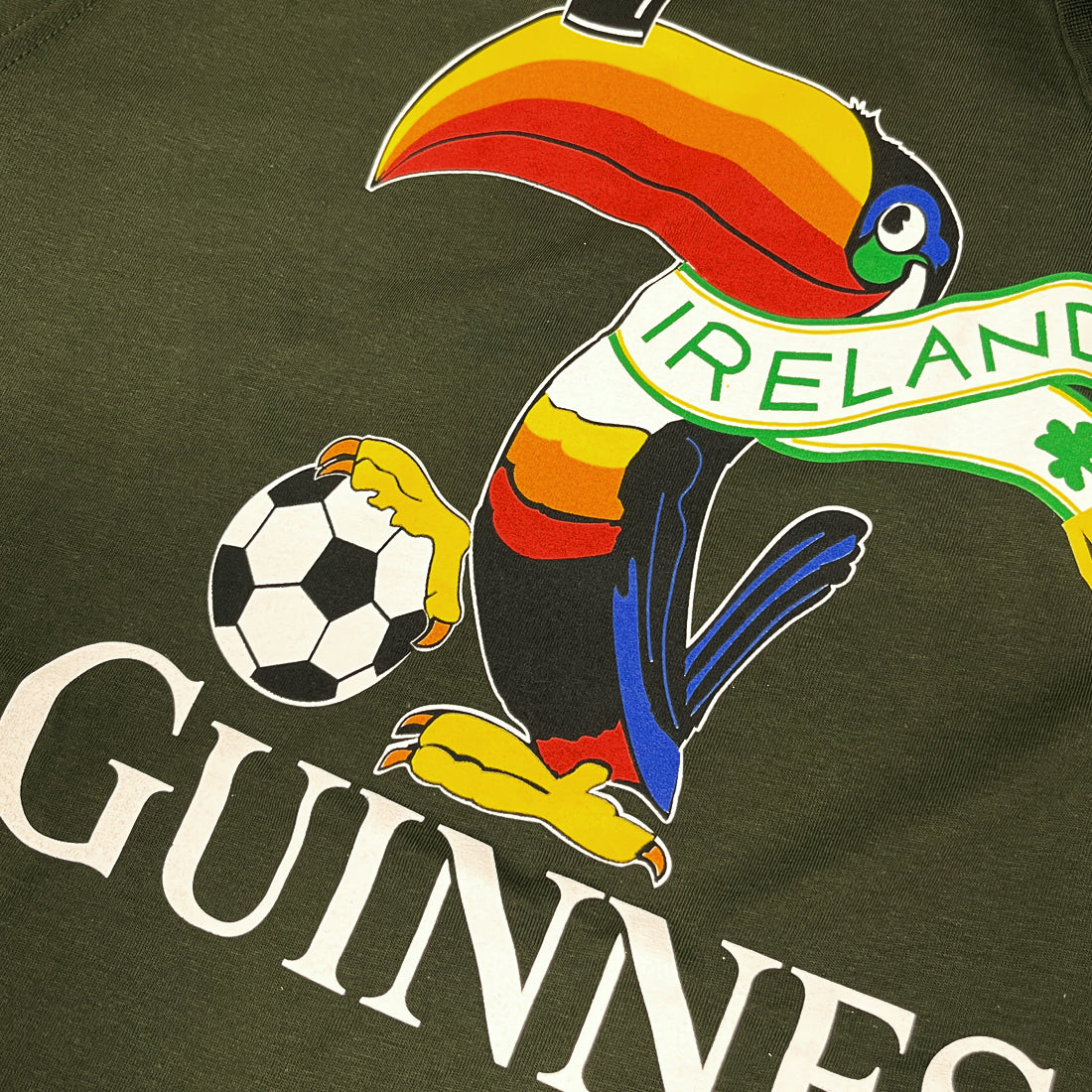 Close-up of the front graphic on the Guinness bottle green T-shirt showing a colorful toucan with a football and Ireland scarf