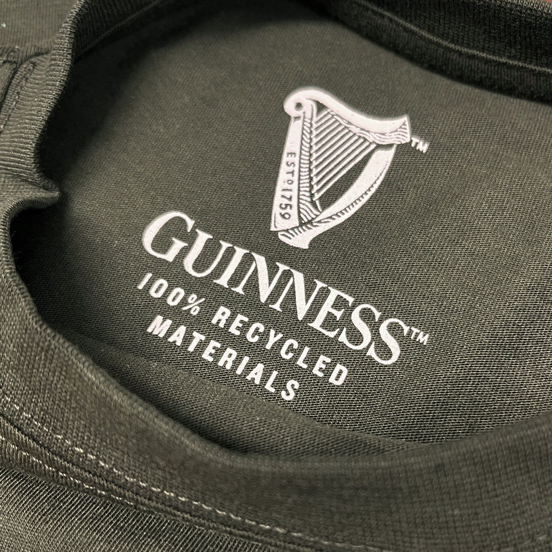 Close-up of the inner neck print on a dark fabric with the Guinness harp logo and the text 100% RECYCLED MATERIALS