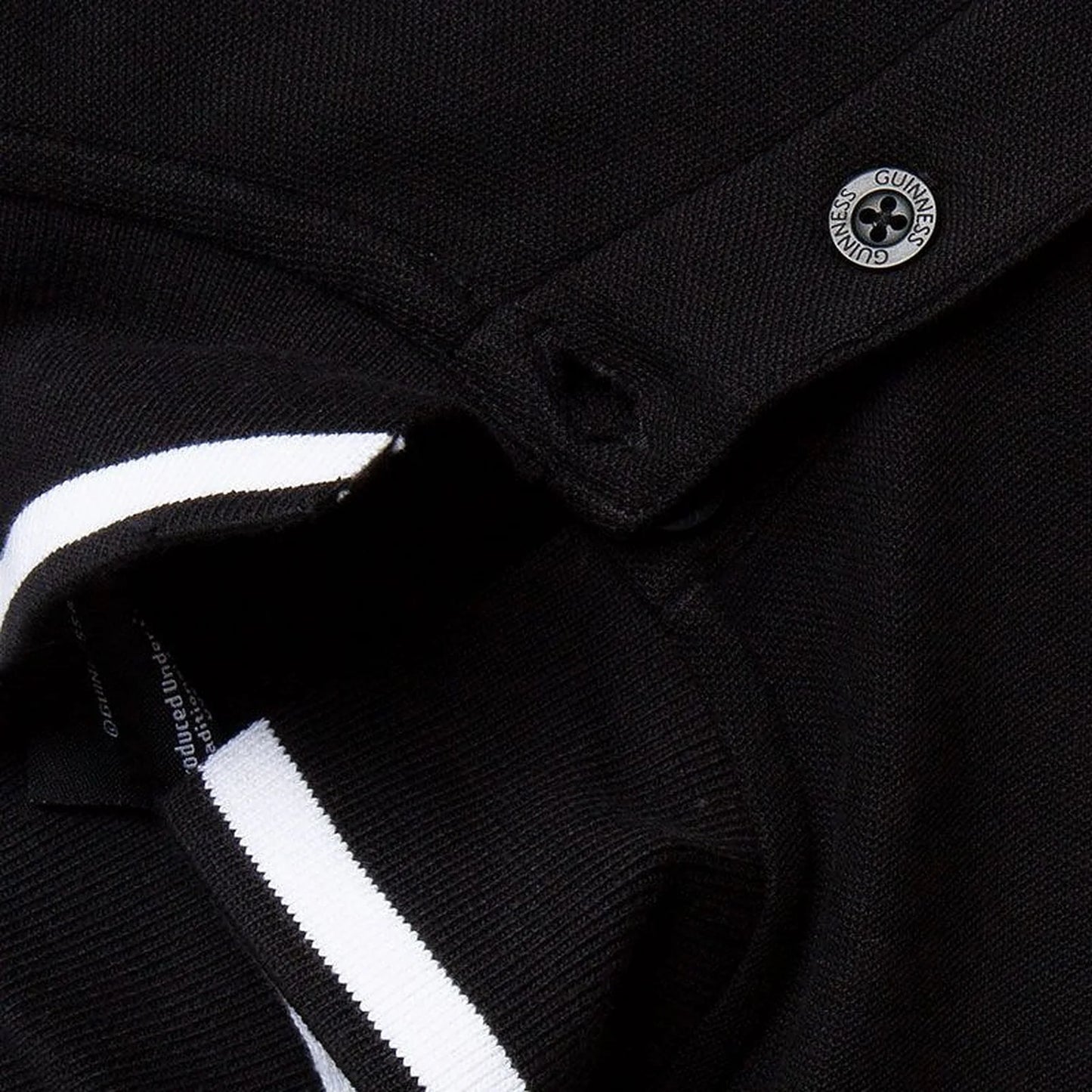 Close up of black Guinness polo showing a metallic crest button and white striped collar