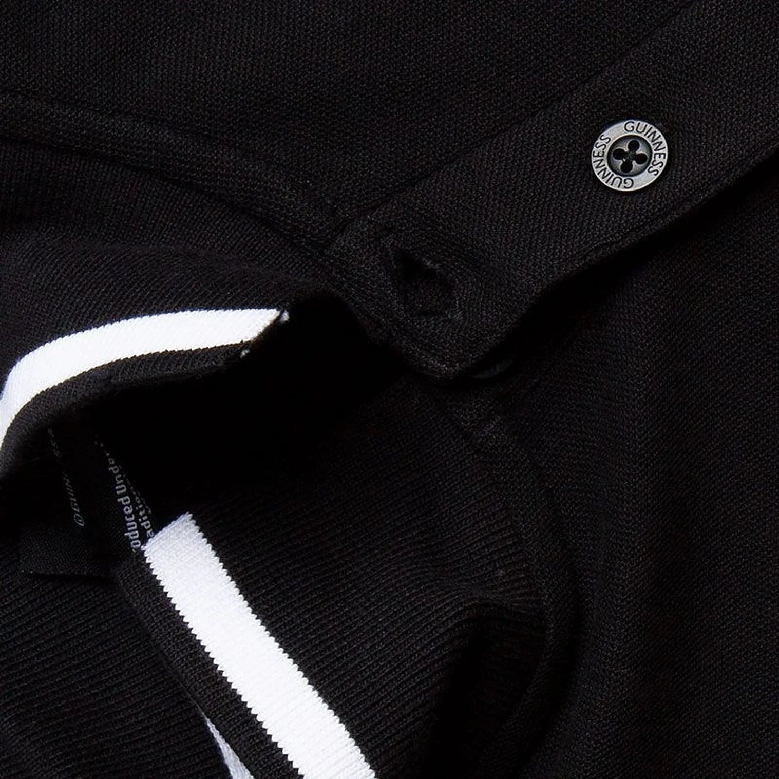 Close up of black Guinness polo showing a metallic crest button and white striped collar