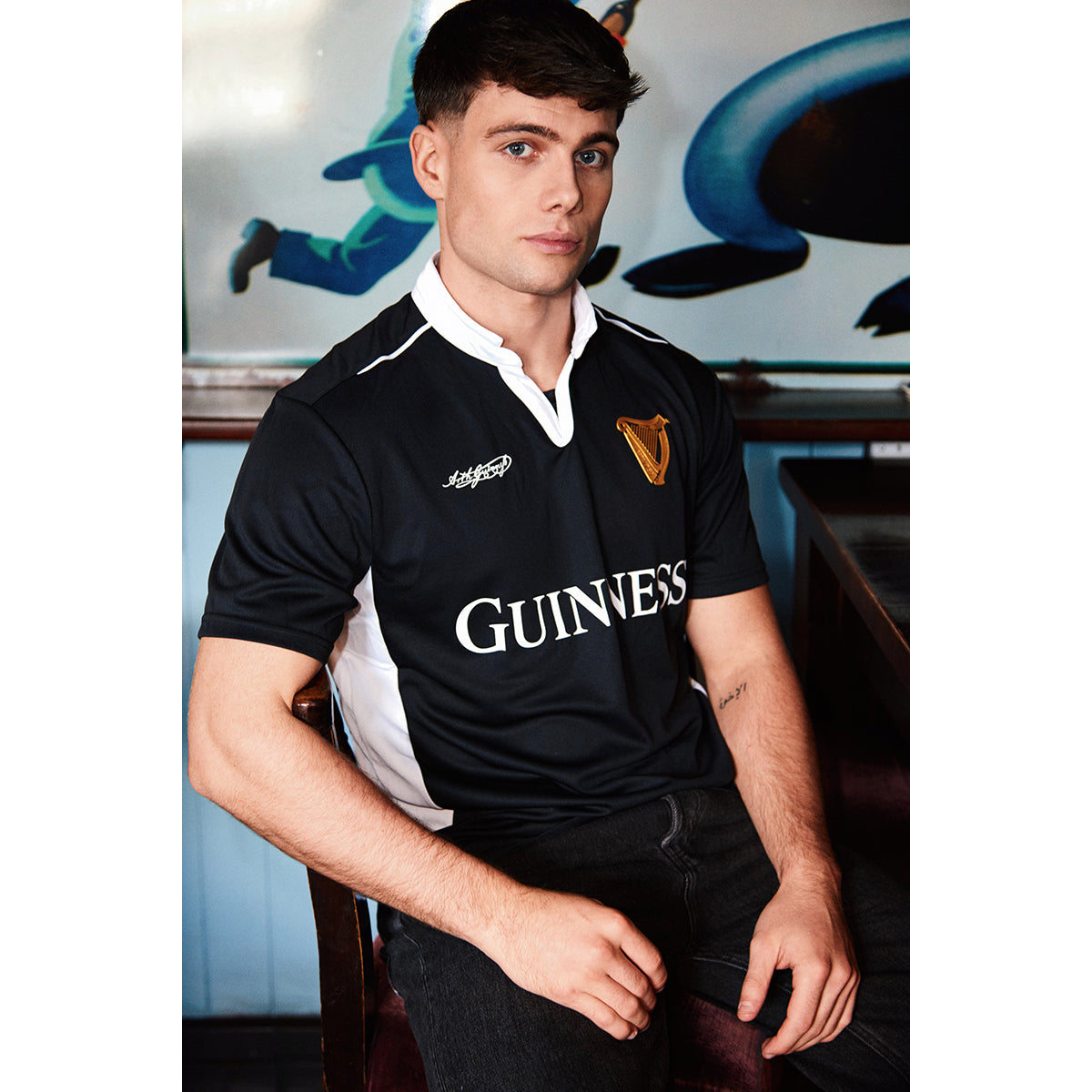 Male model wearing black Guinness performance short sleeve top with white collar trim and gold harp crest.