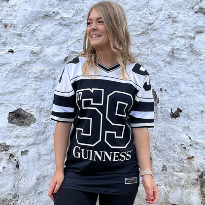 Woman wearing a black and white Guinness football jersey with a large 59 and Guinness logo against a white textured wall.