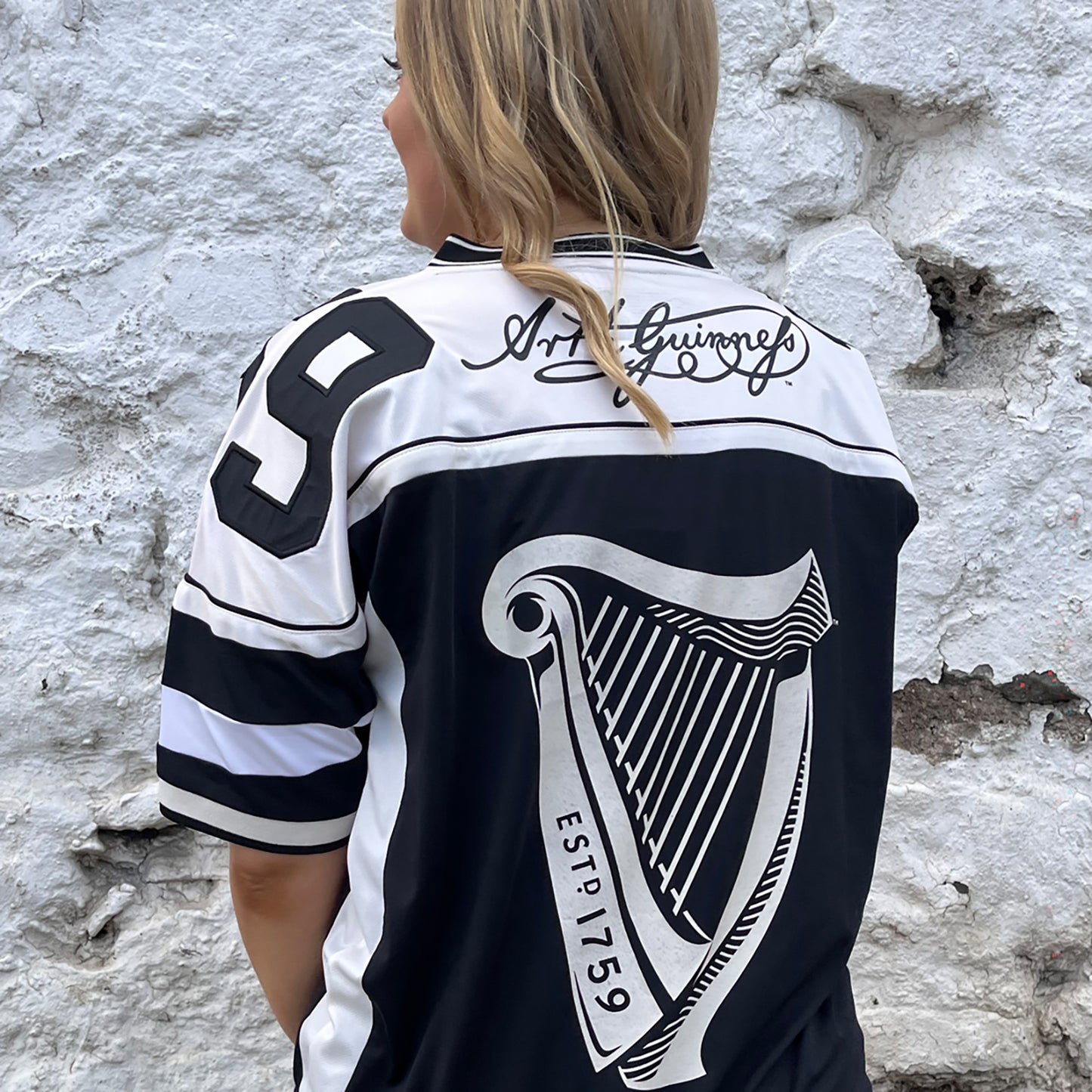 Back view of a Guinness football jersey with a large harp graphic and Art Guinness signature across the shoulders.