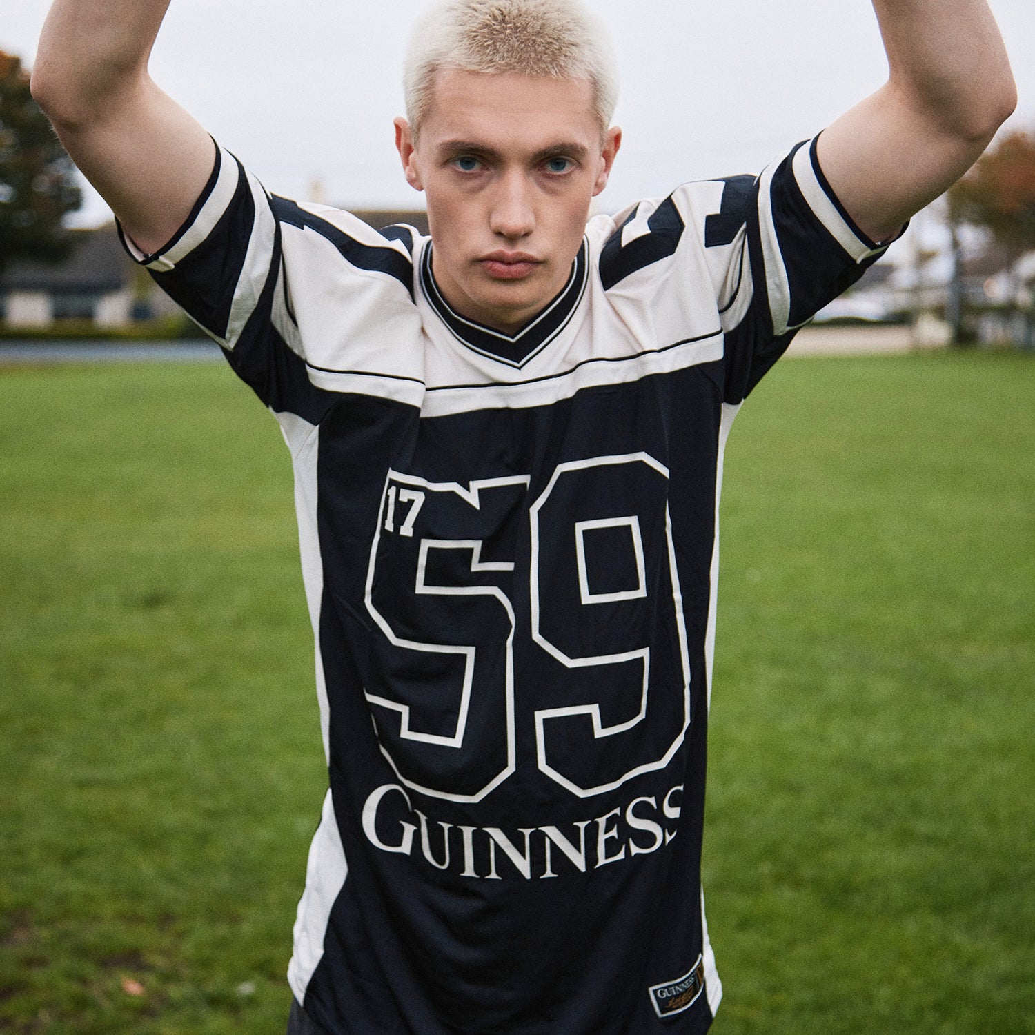 Male model wearing a black Guinness football jersey with white piping and a large 59 on a grassy field.
